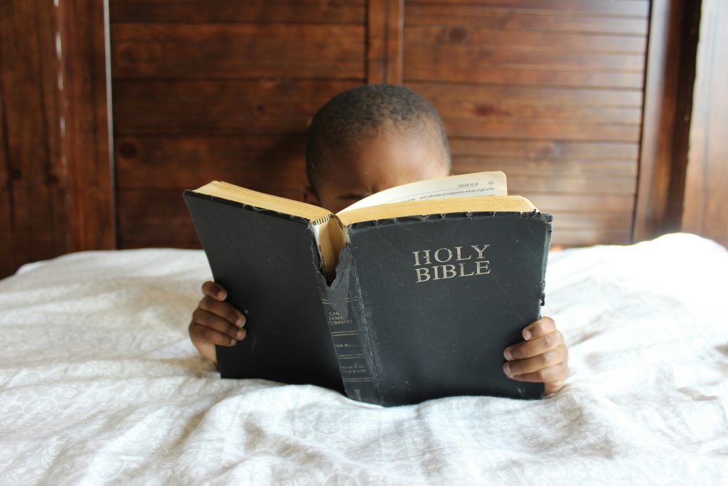 A young child reading The Bible in bed